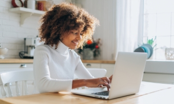 Young lady in yellow shirt looking at laptop smiling